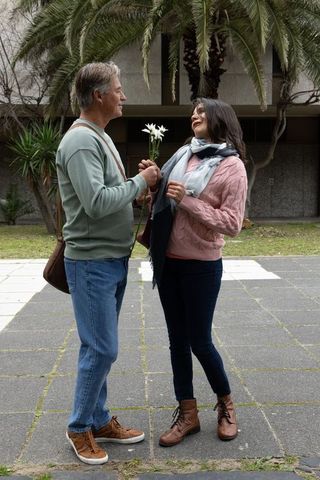 Middle-aged couple exchanging white flowers in city courtyard, romantic outdoor moment