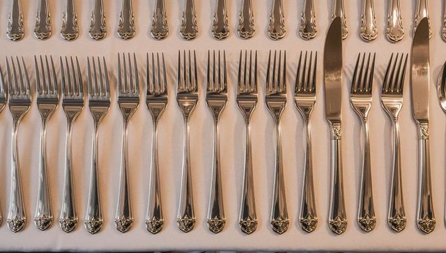 Displaying polished silver flatware lining symmetrical rows on white linen table