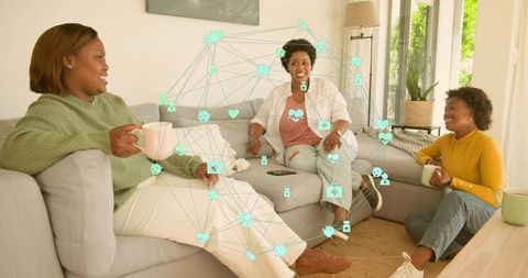 Black Women Chatting on Sofa with Coffee Cups and Smartphone Showing Social Network Overlay