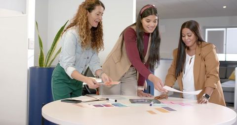 Diverse female colleagues collaborate on color swatch review at office