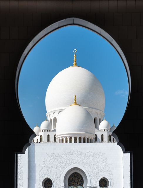 Elegant view emphasizes architectural beauty of mosque domes framed by archway. Ideal for religious, architectural, cultural, travel content, highlighting Islamic arts, spirituality, heritage preservation.