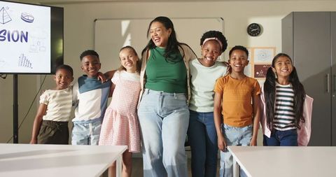 Multiracial teacher laughing with elementary students embracing teamwork and vision