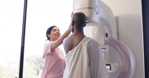 African woman undergoing mammogram while nurse adjusting mammography machine