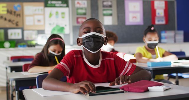 Scene features children wearing masks attentively learning in a classroom, highlighting concepts of modern education during pandemic, health and safety in schools. Useful for materials about education, classroom safety, back to school promotions, and public health guidelines.