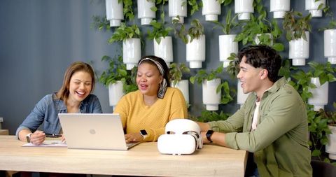Diverse Team Collaborating with Laptop and VR Headset in Modern Green Workspace