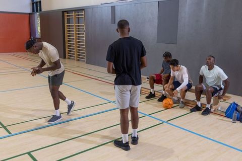 Diverse male teammates preparing for basketball practice in indoor gym bench scene