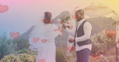 Exchanging rings during romantic outdoor wedding under floral arch with mountain backdrop
