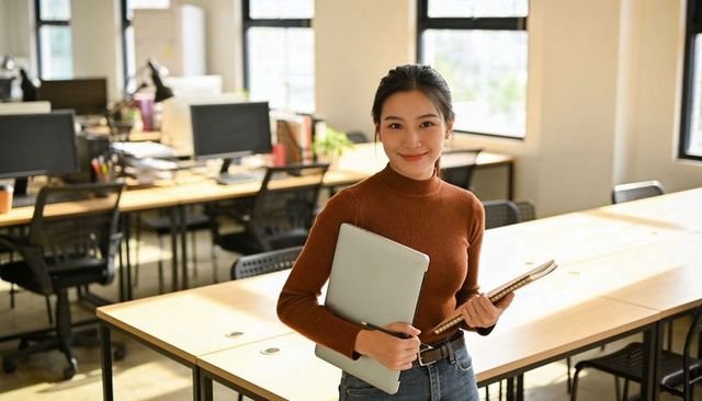 Young professional holding laptop and notebook in bright minimalist coworking space