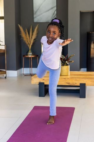 African girl practicing yoga balance pose at home on magenta mat for mindfulness