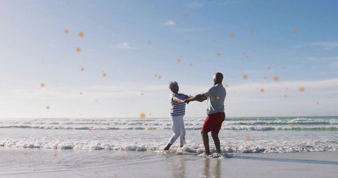 Mature couple holding hands dancing on sunny ocean shoreline with sea foam reflections