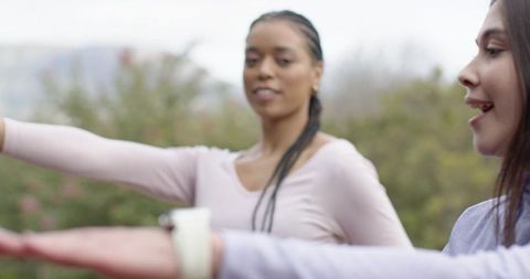 Two women stretching arms forward in park during outdoor workout and balance routine