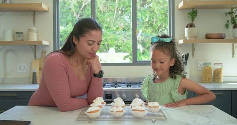 Mother and daughter baking cupcakes on bright kitchen island, family bonding over frosting