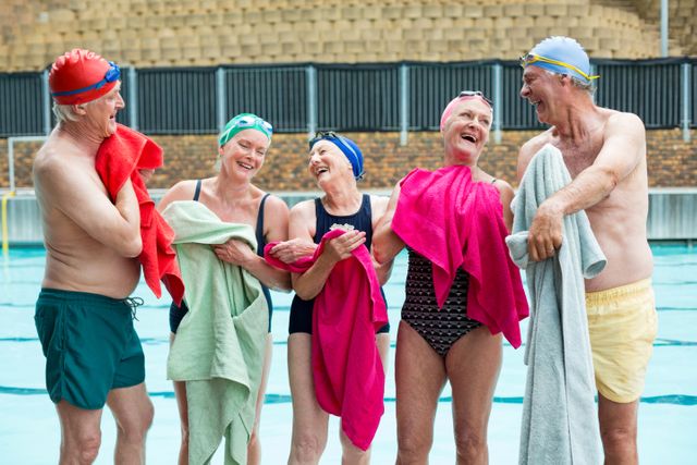 Group of happy senior swimmers wiping body with towels at poolside 