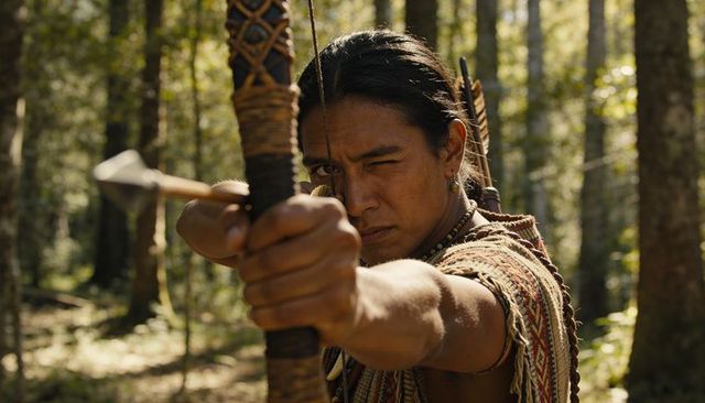 Indigenous archer drawing bow and aiming metal-tipped arrow in sunlit forest