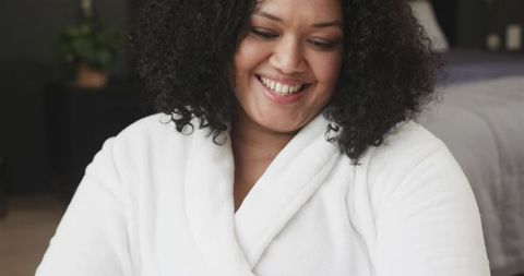 Smiling African American Woman in White Robe Relaxing in Cozy Bedroom Soft Morning Light