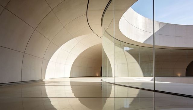 Curved glass atrium with circular skylight, minimal concrete geometry and soft reflections