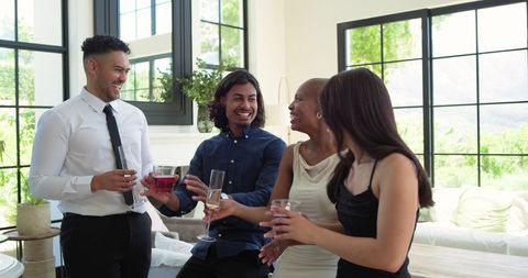 Clinking glasses laughing diverse friends celebrating in bright modern living room