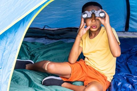African american boy exploring with binoculars inside blue tent on camping trip