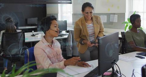 Supervisor coaching call center agent at desktop workstation, teamwork and training