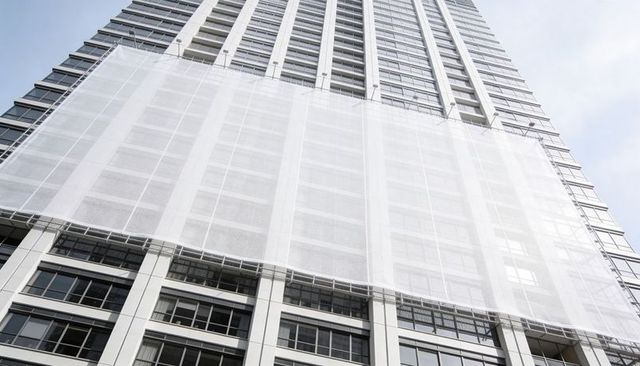 High-rise tower undergoing facade repair showing white scaffold mesh and glass panels