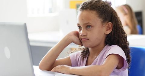 Preteen African American girl studying on laptop in classroom with thoughtful expression