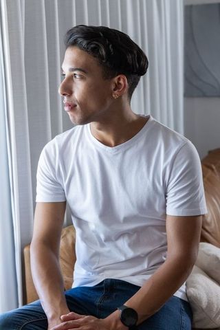 Young man sitting on sofa looking out window wearing white t-shirt in minimalist lounge