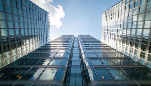 Twin curved glass towers rising into bright blue sky with reflective modern office facade