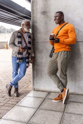 African american men chatting and laughing at concrete plaza with coffee and smartphones