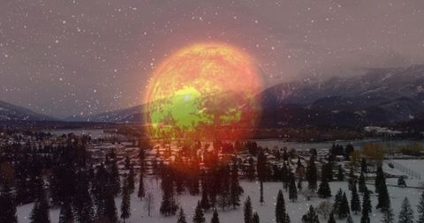 Glowing green-patched orange orb hovering over snowy mountain town at dusk casting warm light