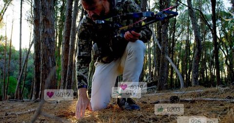 Kneeling hunter inspecting forest floor holding compound bow with media likes overlay