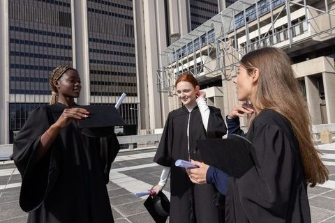 Diverse female graduates celebrating on urban rooftop terrace holding caps and diplomas