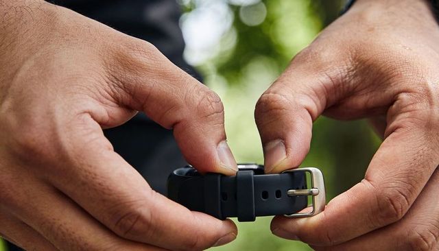Hands fastening black silicone watch strap with metal buckle macro closeup outdoor detail