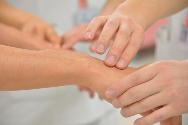 Healthcare professionals are pressing fingers on a patient's wrist to check their pulse. Useful for medical articles, healthcare training materials, nursing manuals, and first aid guides.