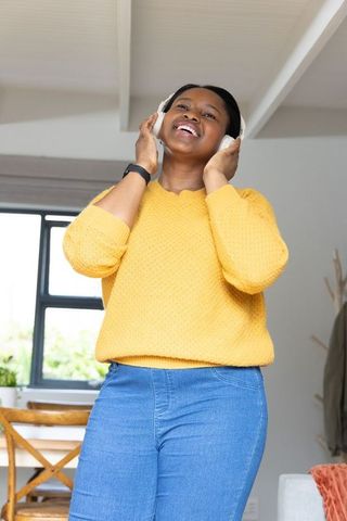 African american woman singing with headphones in mustard sweater at home