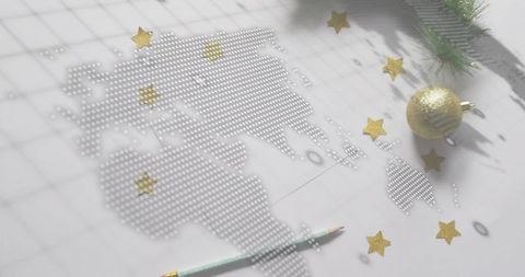 Perforated dot world map with gold bauble, stars and mint pencil for holiday planning