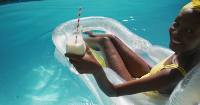Young woman in bright swimsuit floating on an inflatable pool lounge while enjoying a refreshing beverage. Ideal for use in articles about summer activities, relaxation, poolside leisure, vacationing, and lifestyle imagery.