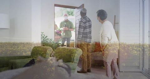 Masked delivery bringing flowers and package at open door welcoming older couple at home
