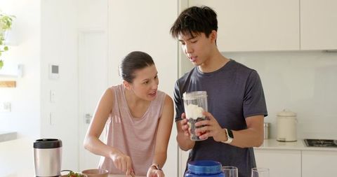 Multicultural couple making protein smoothie in bright modern kitchen for wellness
