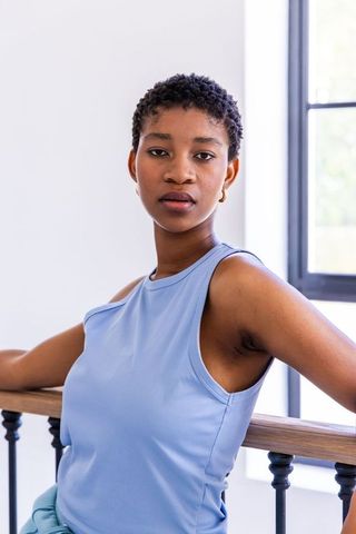 African american woman standing at railing in sunlit room wearing blue sleeveless top