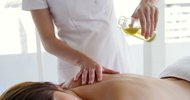 A massage therapist is applying oil to a client's back during a therapy session, with copy space. Capturing a moment of relaxation and wellness, the image reflects the therapeutic industry and self-care practices.
