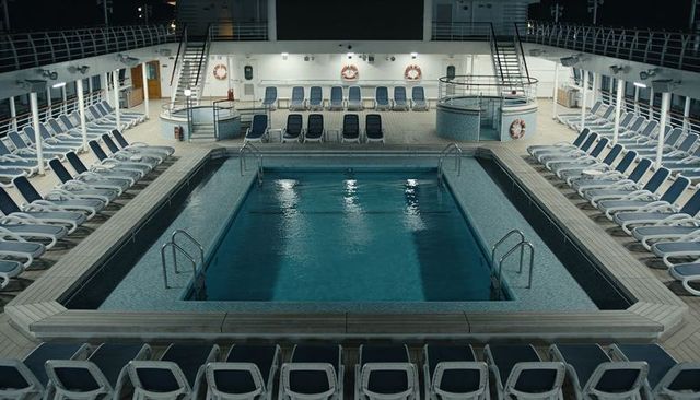 Empty cruise ship pool deck at night with symmetrical sunbeds, reflective water, modern design