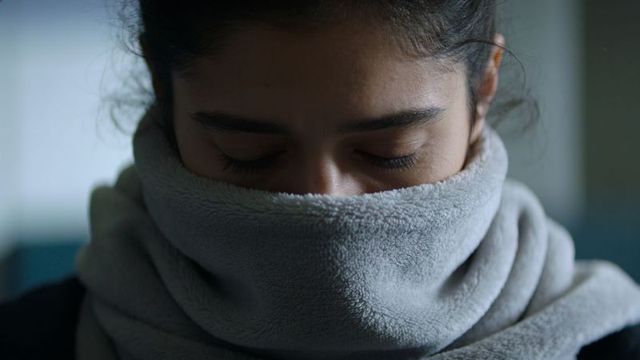 Woman resting wrapped in light-gray fleece scarf with eyes closed in dim soft light