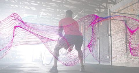 Athlete training with battle ropes in industrial warehouse gym, backlit silhouette with magenta moti
