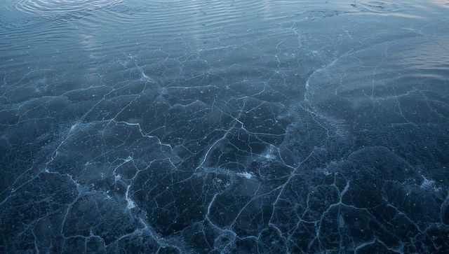 Revealing cracked ice patterns on frozen lake surface with frosty blue texture and bubbles