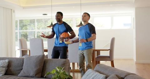 Diverse friends cheering in modern open-plan living room wearing matching blue shirts