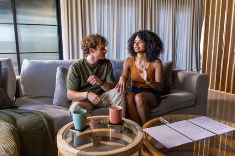 Young couple reviewing documents on sofa with coffee mugs in modern cozy living room
