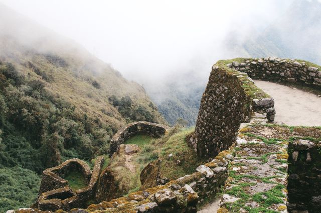 Ancient Inca ruins on a mountain enveloped in mist, showcasing stone walls and verdant surroundings. Ideal for content related to travel, history, archaeology, ancient civilizations, and scenic landscapes.