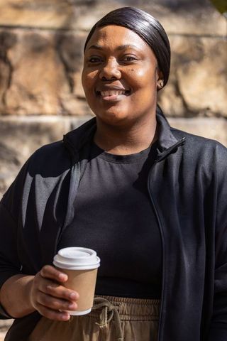 African american woman smiling with coffee cup urban sunlight athleisure portrait friendly