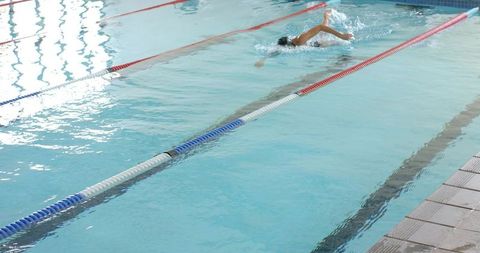 Female swimmer training freestyle laps in indoor pool with lane ropes and reflections