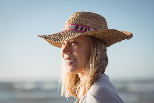 Happy woman looking away while wearing sun hat at beach during sunny day